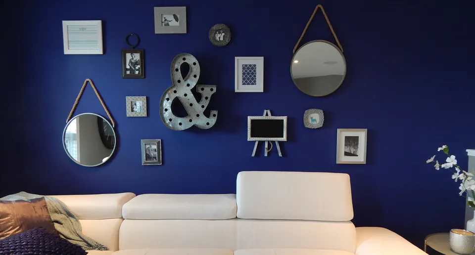 A deep navy accent wall behind a white sofa, styled with mirrors and art