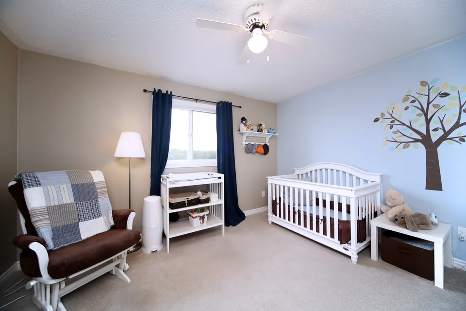 A nursery with a soft blue wall and a painted tree mural