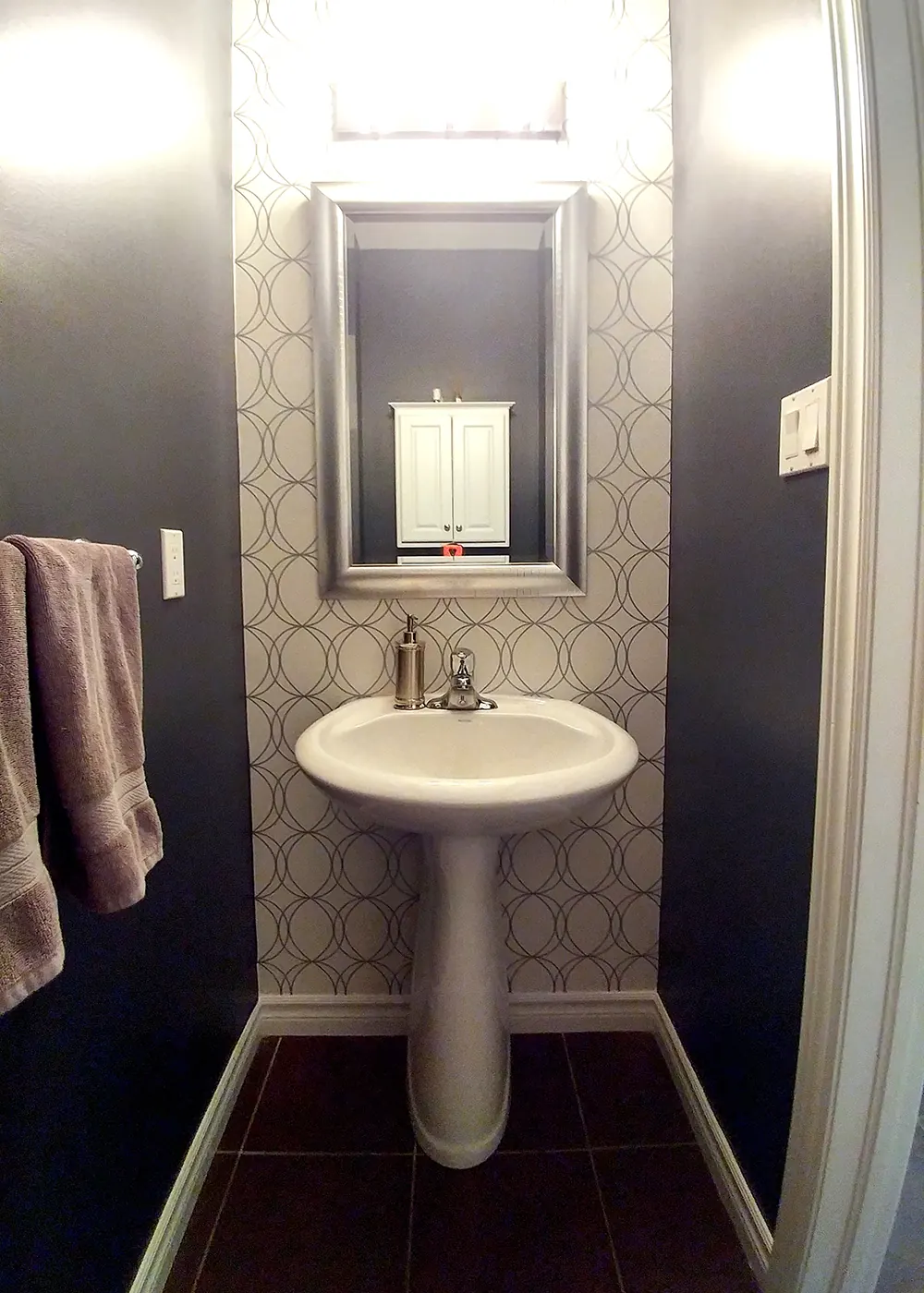A powder room with a navy wall beside patterned wallpaper